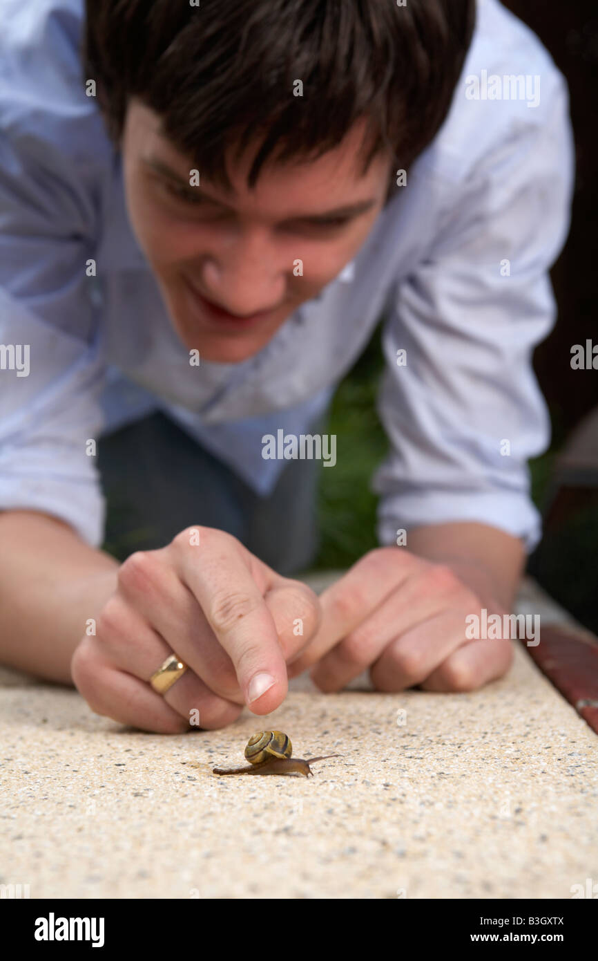 young adult male teenager pointing at a snail moving on a garden patio Stock Photo