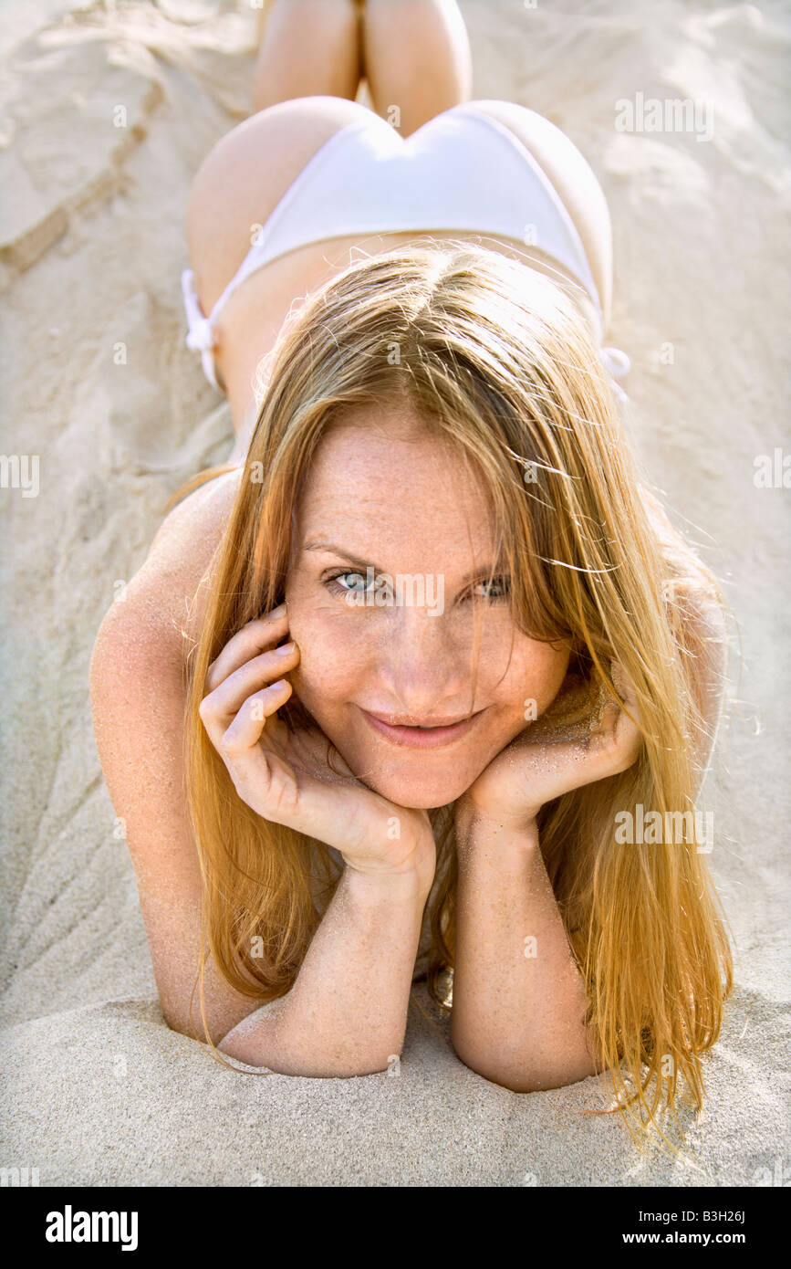 Portrait of pretty redheaded female lying in sand wearing bikini Stock Photo