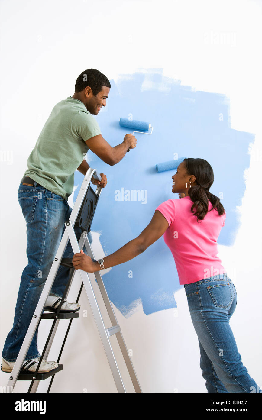 Smiling African American male and female couple painting wall blue Stock Photo