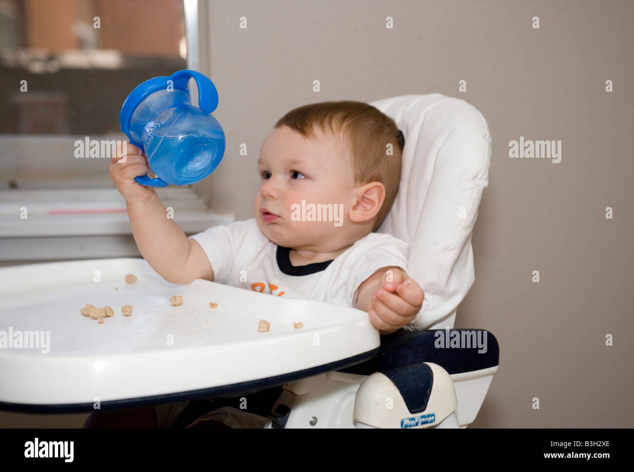 seven month old baby boy holding sippy cup with water, sitting in high
