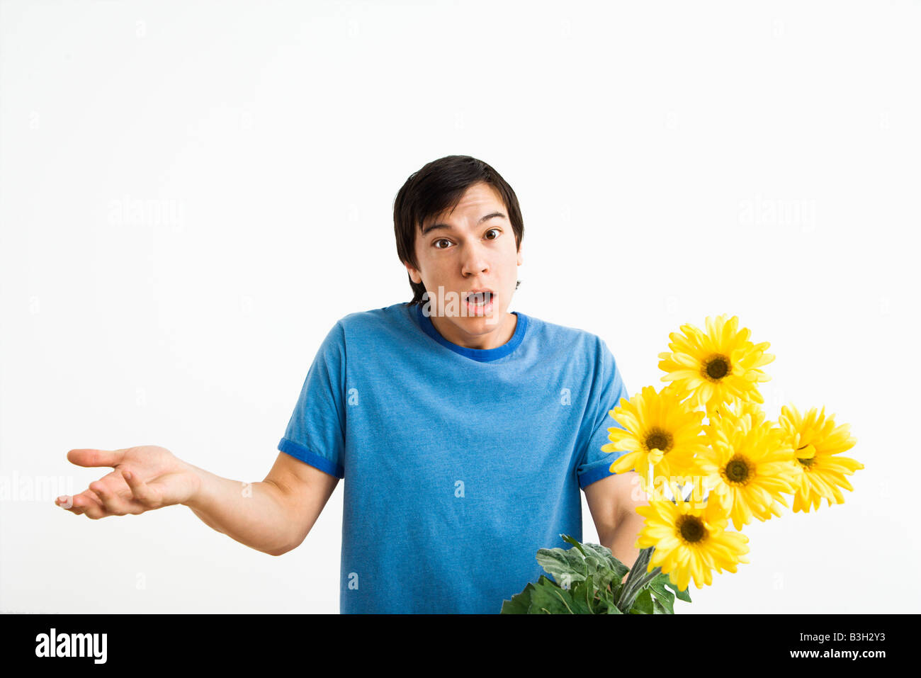 Asian young man holding bouquet of yellow gerber daisies shrugging Stock Photo