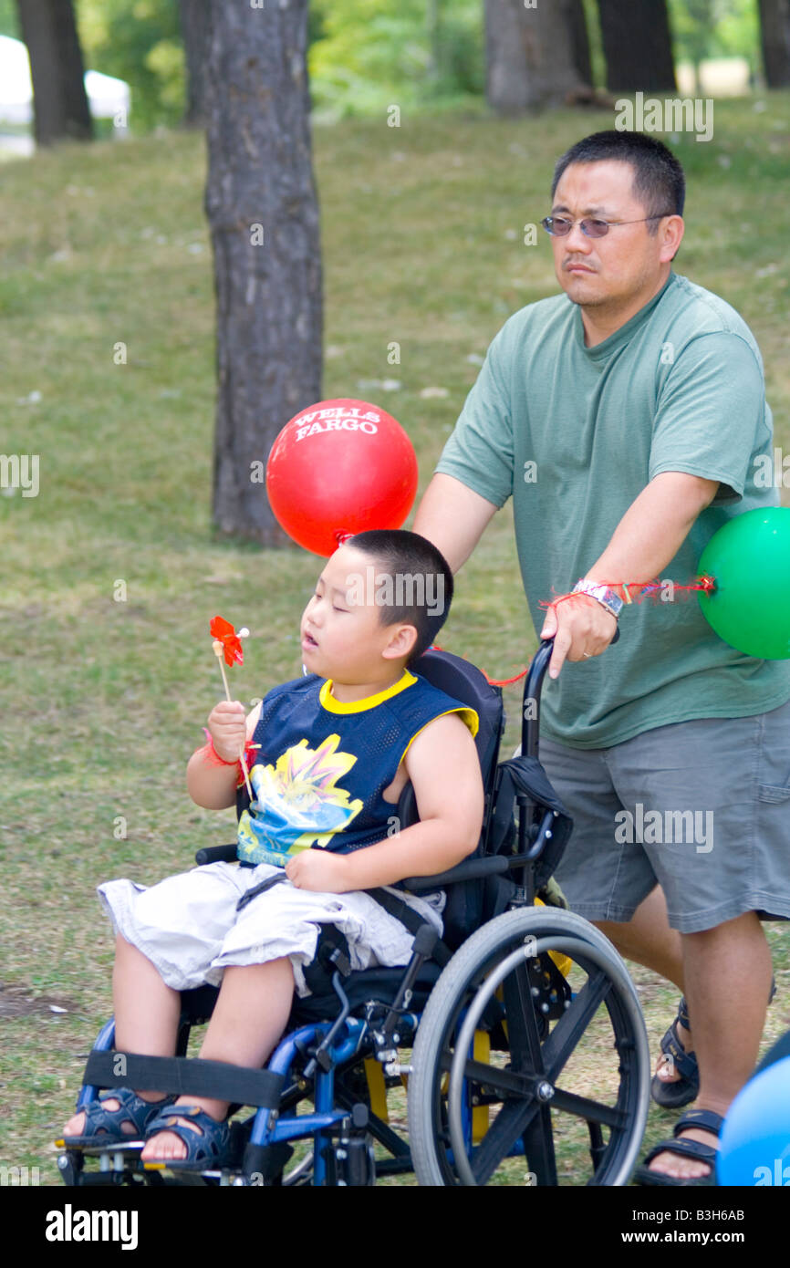 Handicapped physically challenged boy being pushed by dad in wheelchair.  Dragon Festival Lake Phalen Park St Paul Minnesota USA Stock Photo - Alamy