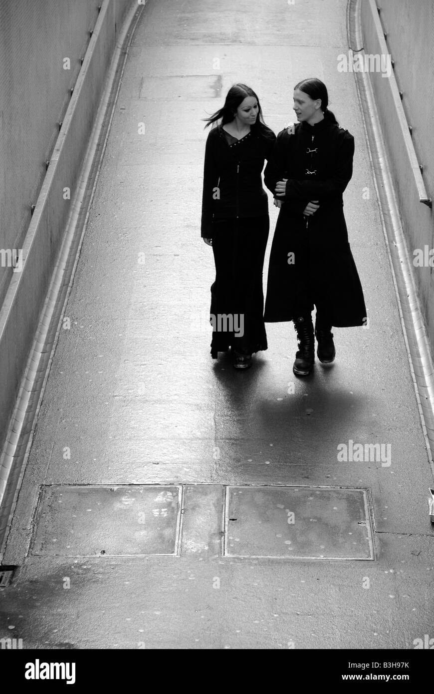 A young teenage goth couple walking arm in arm down into a city underpass Stock Photo