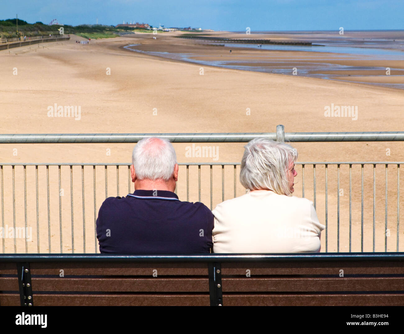 Senior couple tourists enjoying the view on the beach from Skegness Pier, from behind, Lincolnshire, England UK Stock Photo