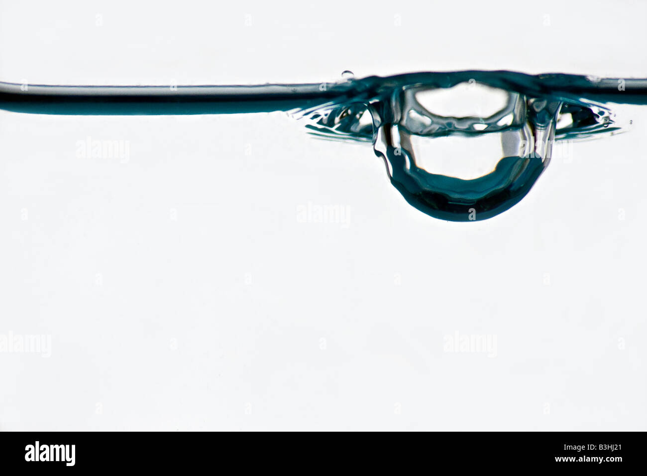 Water drop photographed from below hitting the surface of the water