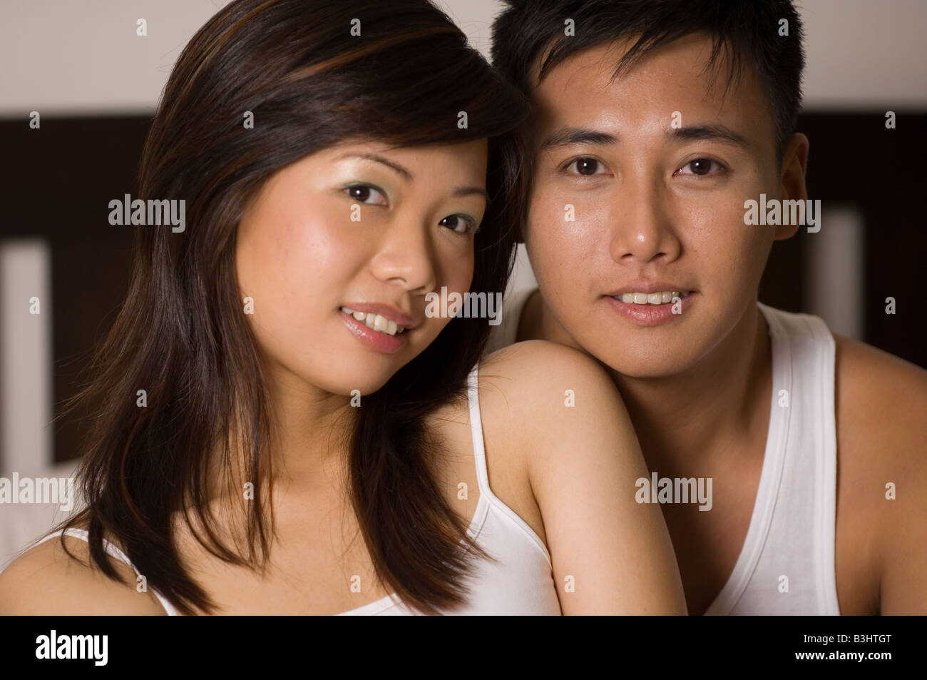A happy looking asian couple pose on a bed inside Stock Photo Alamy