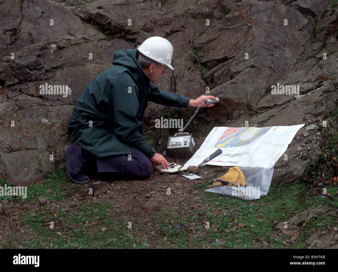 A geologist uses a geiger counter to check for radiation while examining rocks Stock Photo