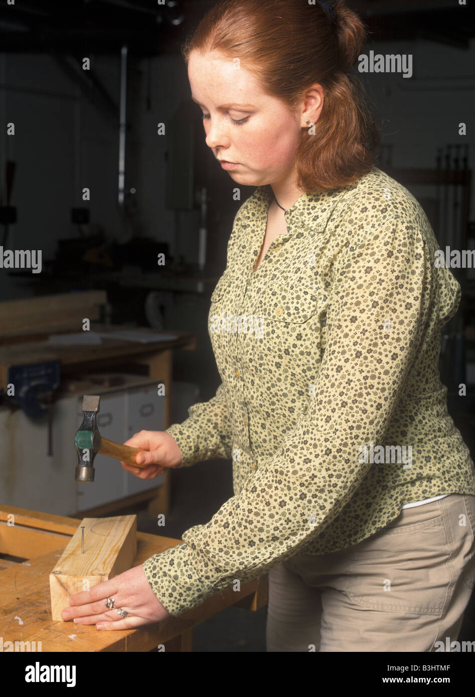 A female student hammers a nail into a piece of wood in a workshop converting energy while she does it Stock Photo