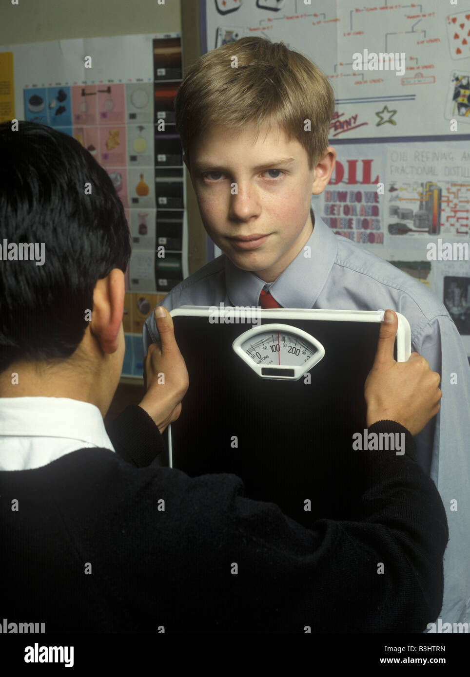 Two schoolboys measure the force of pushing using bathroom scales calibrated in Newtons Stock Photo