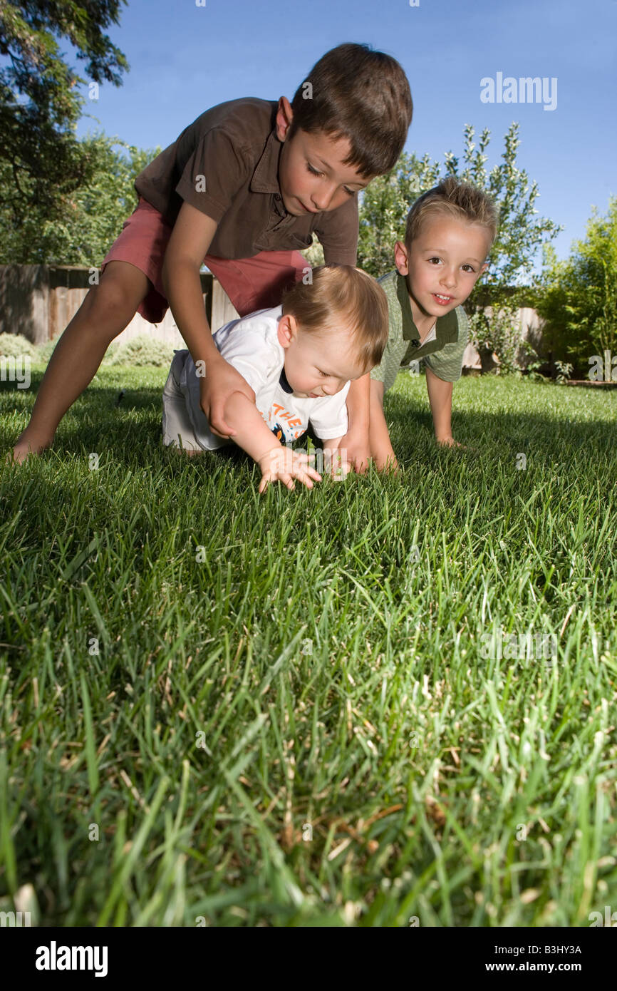 six year old brother and four year old brother help seven month old baby crawl outside in the grass Stock Photo