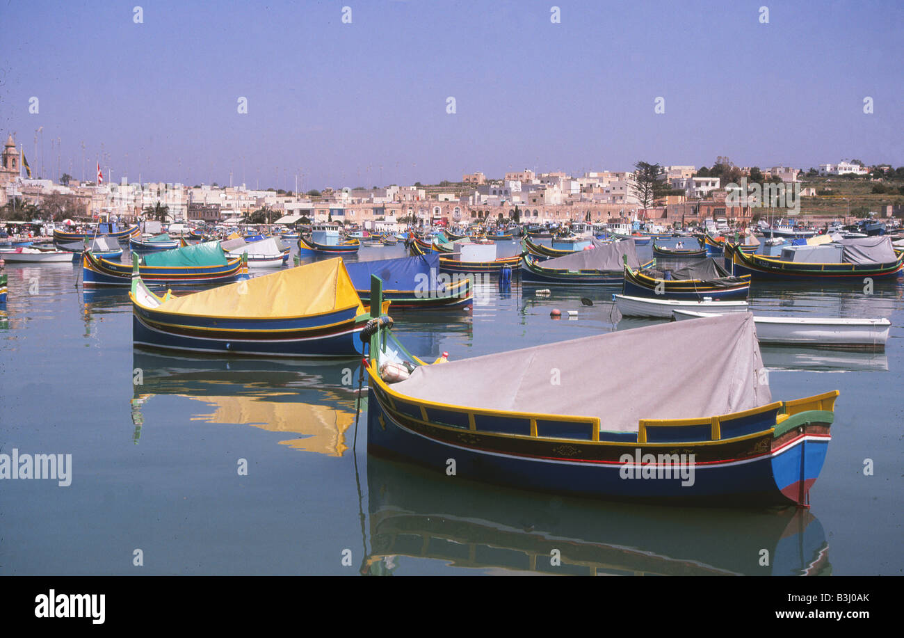 vividly coloured fishing boats in harbour in malta with buildings and ...