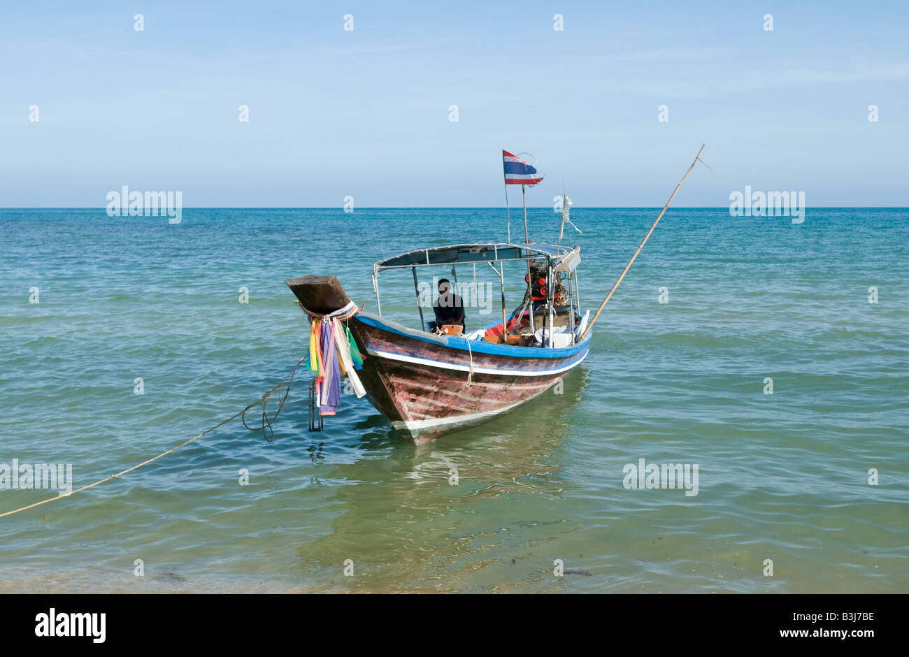 A thai fisherman sits in his boat, moored to the beach at Lamai Koh Samui Thailand Stock Photo