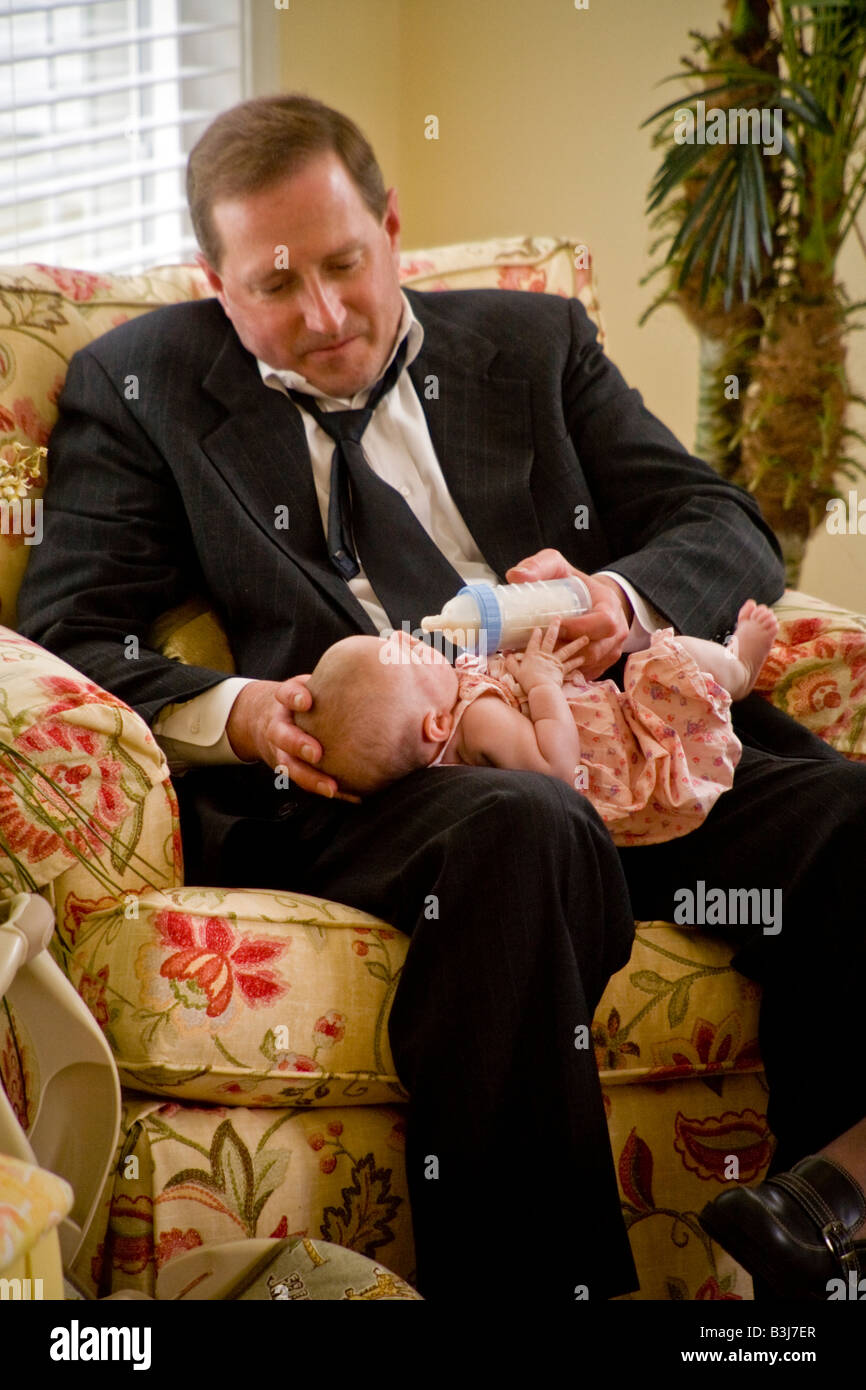 Wearing a look of committed concern an over 40 Irish American man bottle feeds his infant daughter MODEL RELEASE Stock Photo