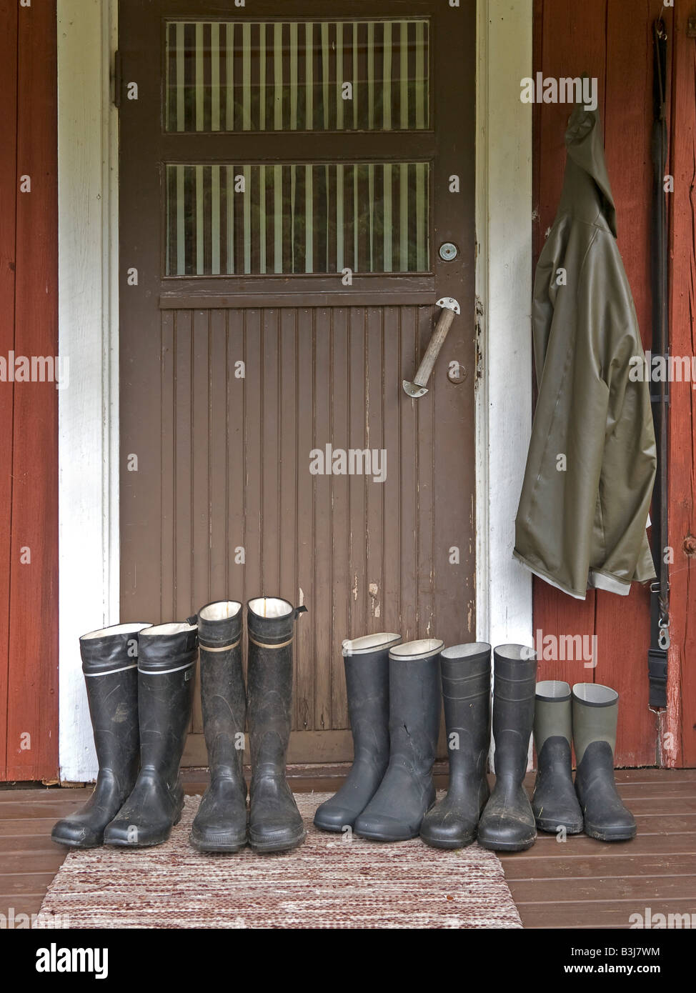 row of rubber boots in front of door of a typical red timber wooden house in Finland Stock Photo