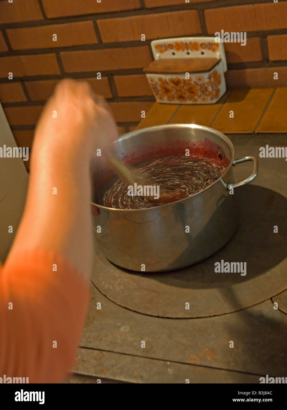 cooking jam in a steal pot stiring sugar with berries hand in movement