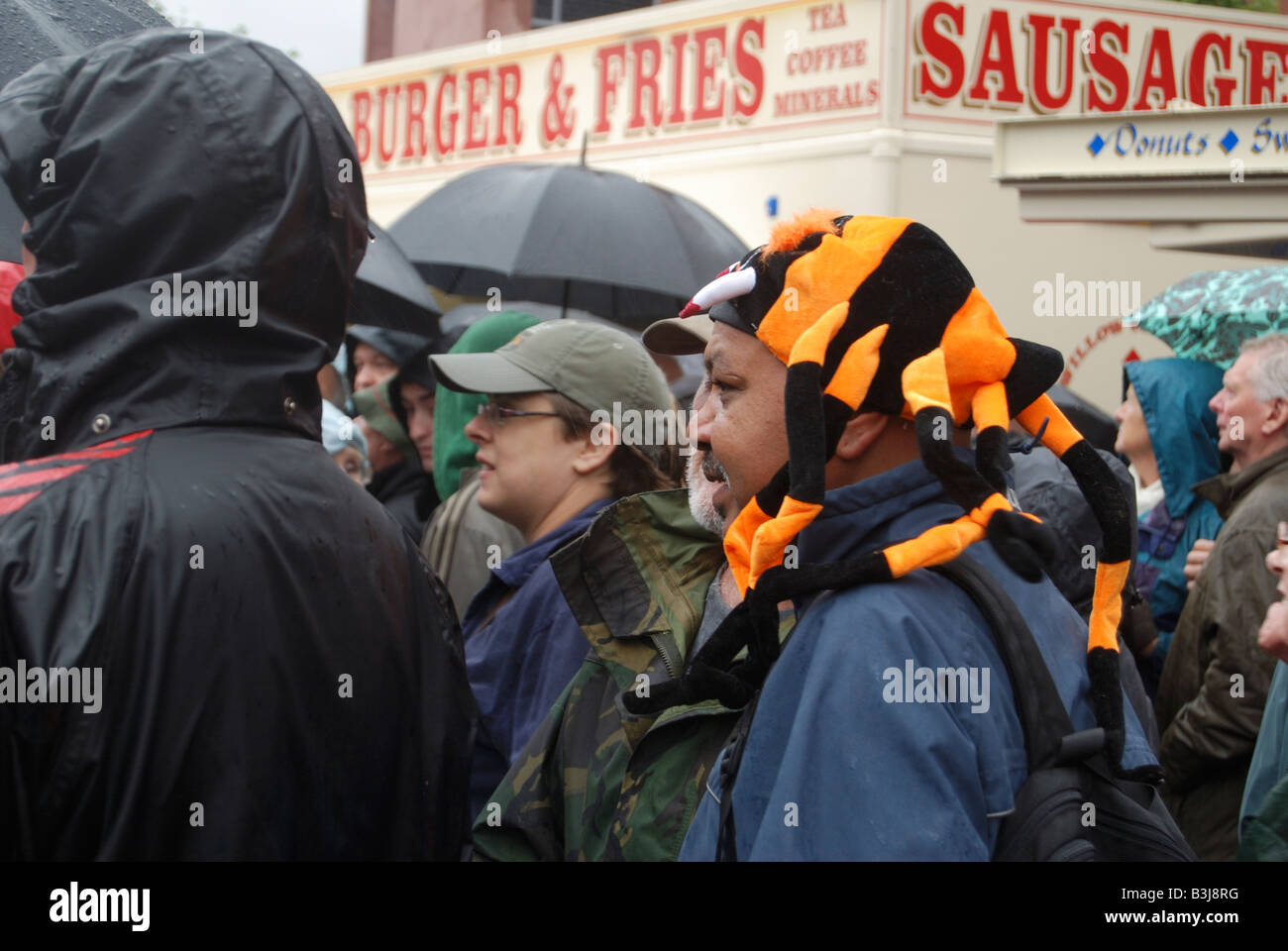 man in crowd wearing a orange and black spider shaped hat Stock Photo