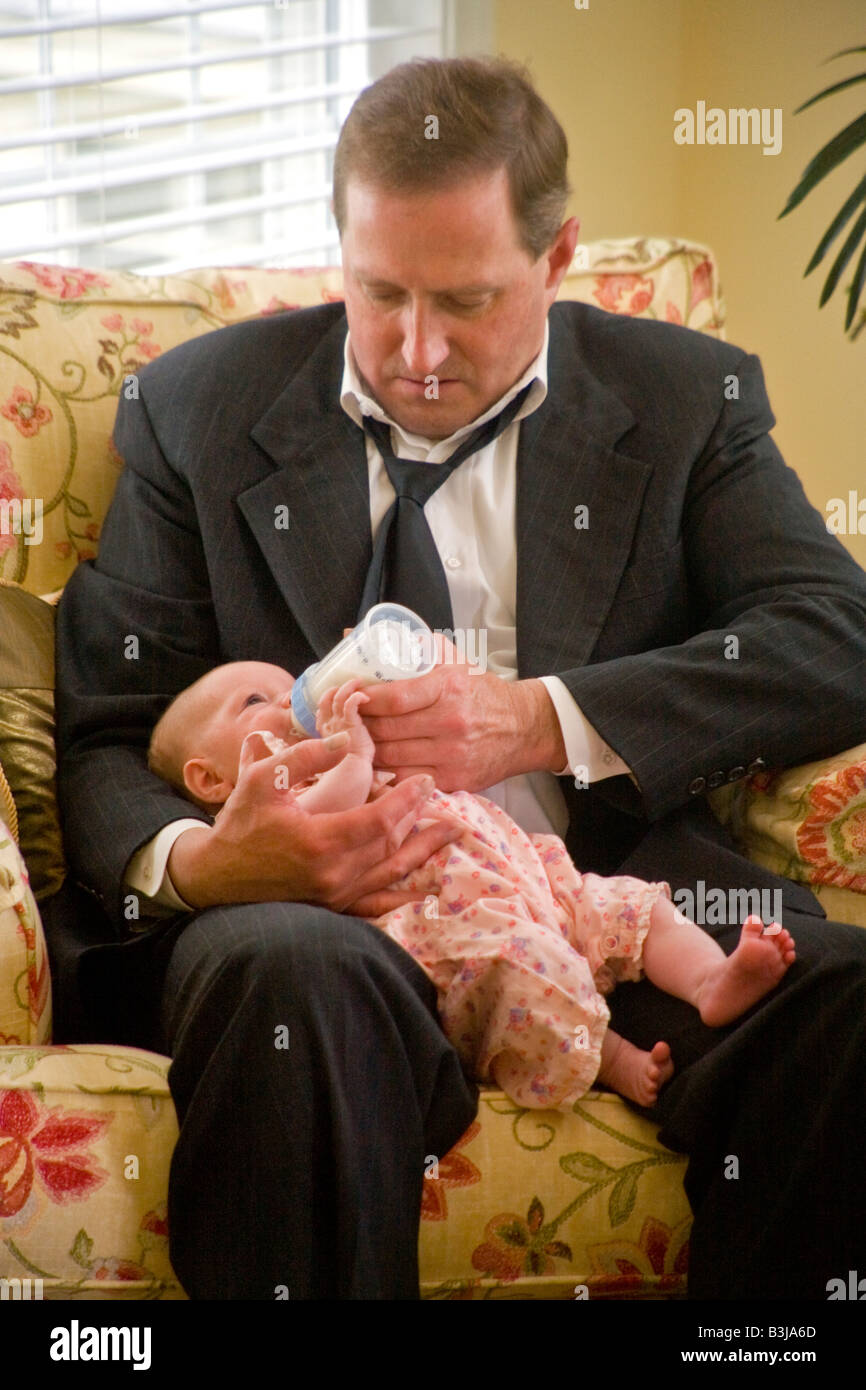 Wearing a look of committed concern an over 40 Irish American man bottle feeds his infant daughter MODEL RELEASE Stock Photo