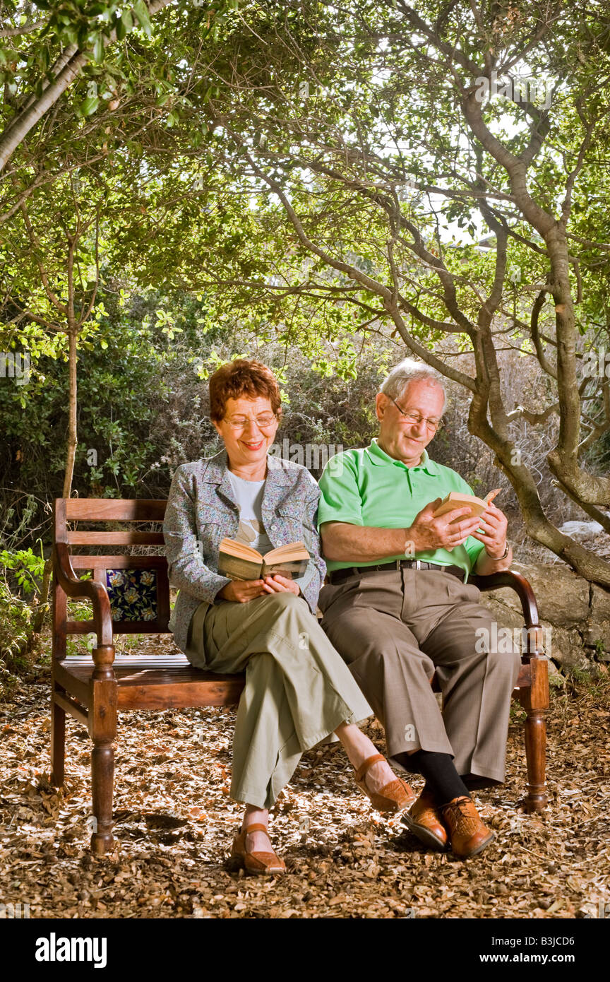 seniors couple sitting on a bench reading books in the park Stock Photo ...