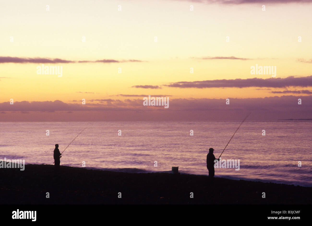 2 Two silhouettes of people surf fishing at sunrise over Misquamicut Beach in Westerly, Rhode Island USA. Stock Photo