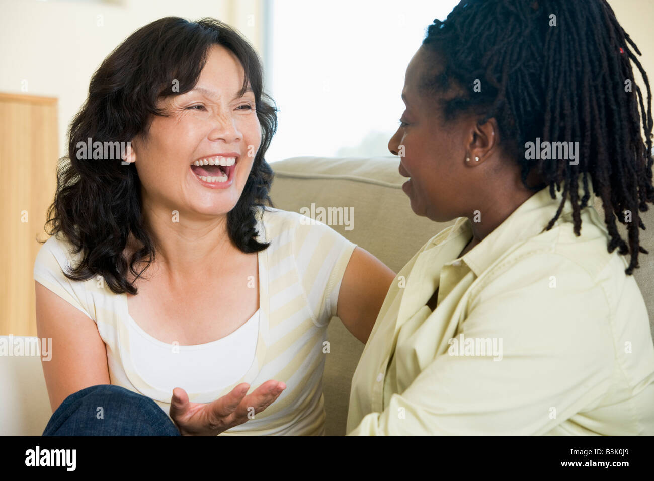 Two women talking in living room and smiling Stock Photo