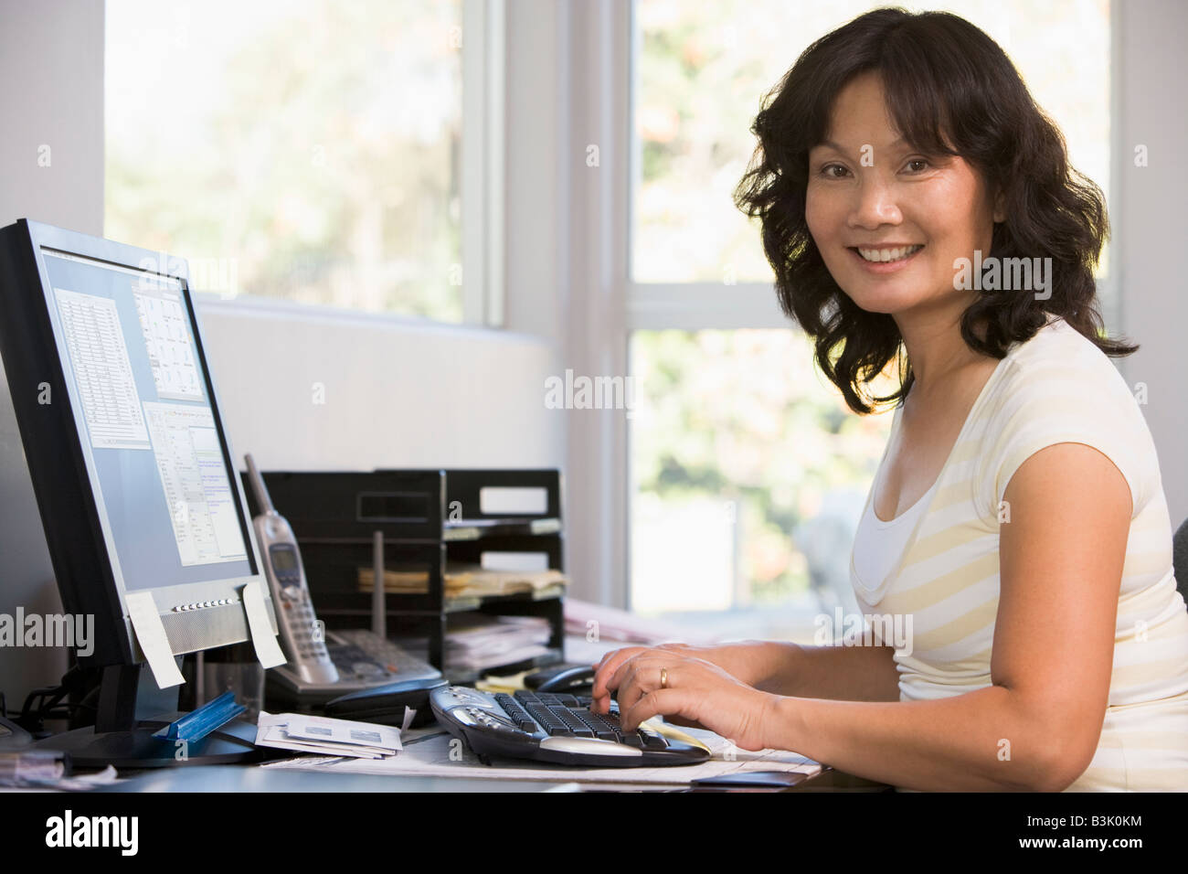 Woman in home office using computer and smiling Stock Photo - Alamy