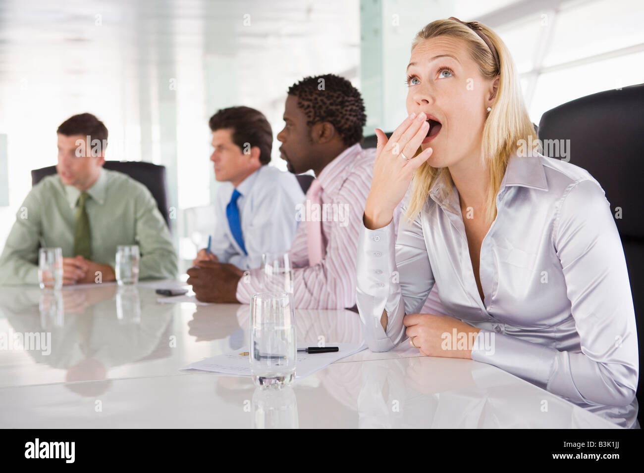 Four businesspeople in boardroom with one businesswoman yawning Stock Photo