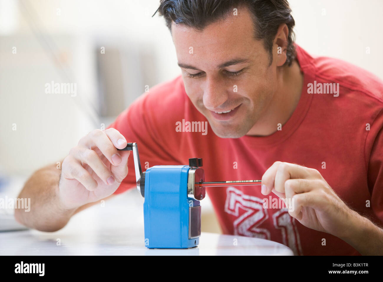 Man indoors using pencil sharpener smiling Stock Photo