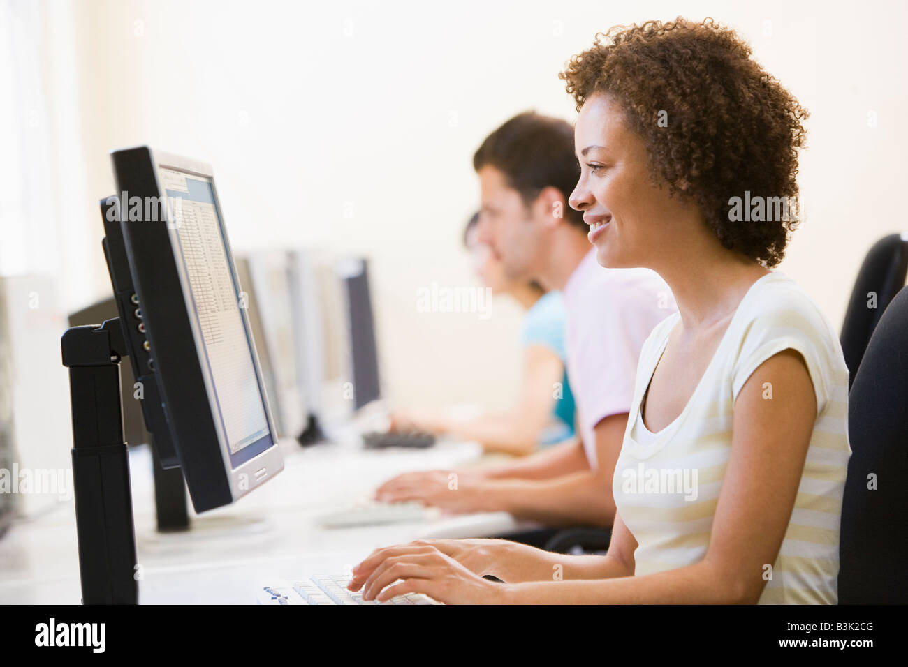 Three people sitting in computer room typing and smiling Stock Photo