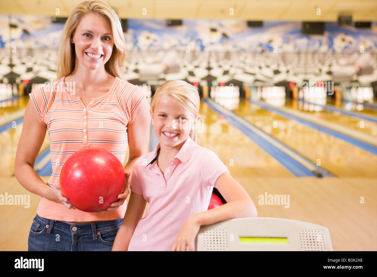 Woman and young girl in bowling alley holding ball and smiling Stock Photo