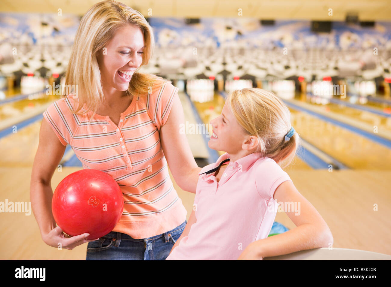 Woman and young girl in bowling alley holding ball and smiling Stock Photo