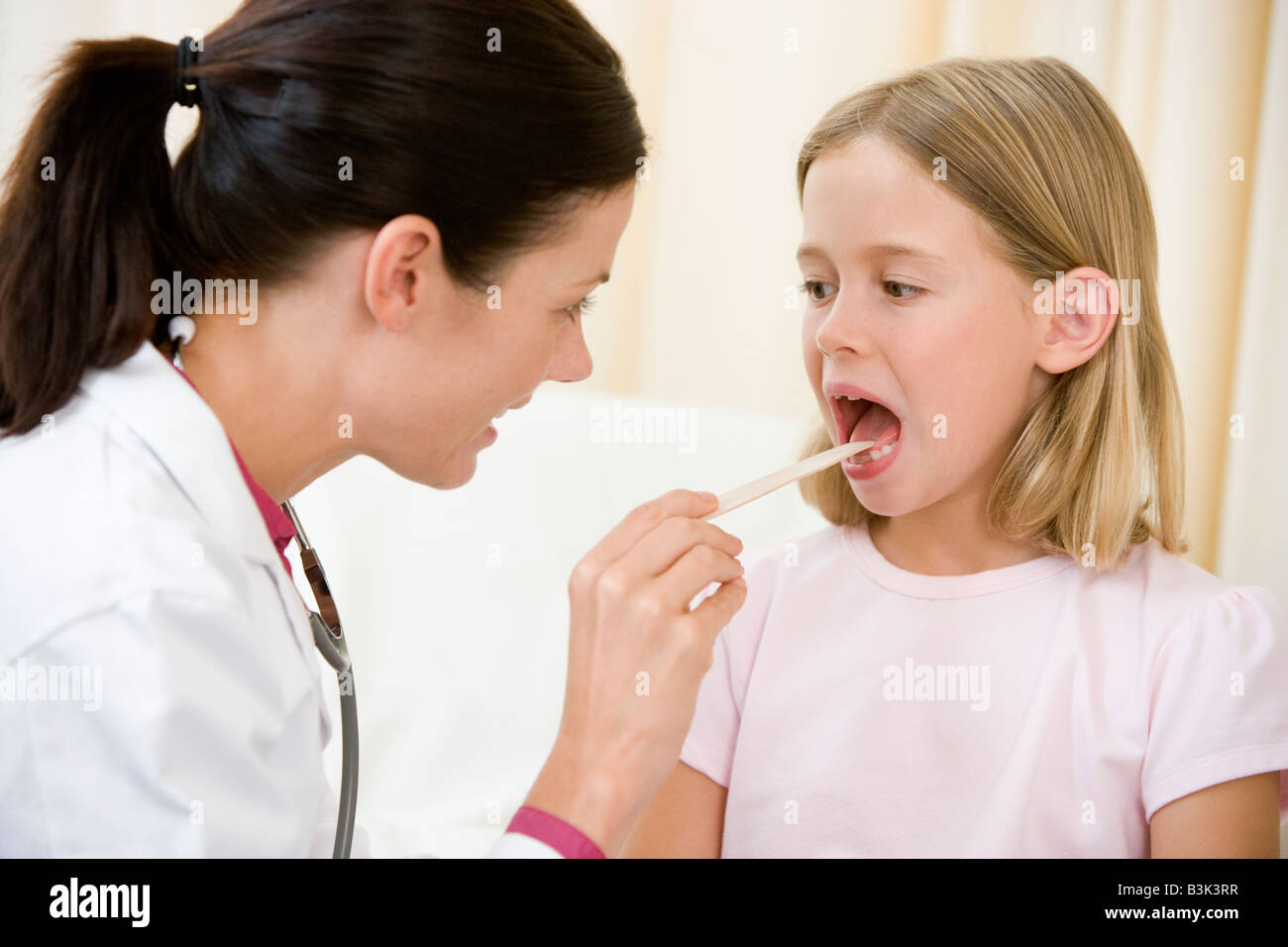 Doctor giving checkup to young girl with tongue depressor in exam room