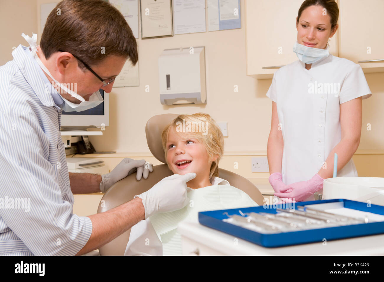 Dentist and assistant in exam room with young boy in chair Stock Photo