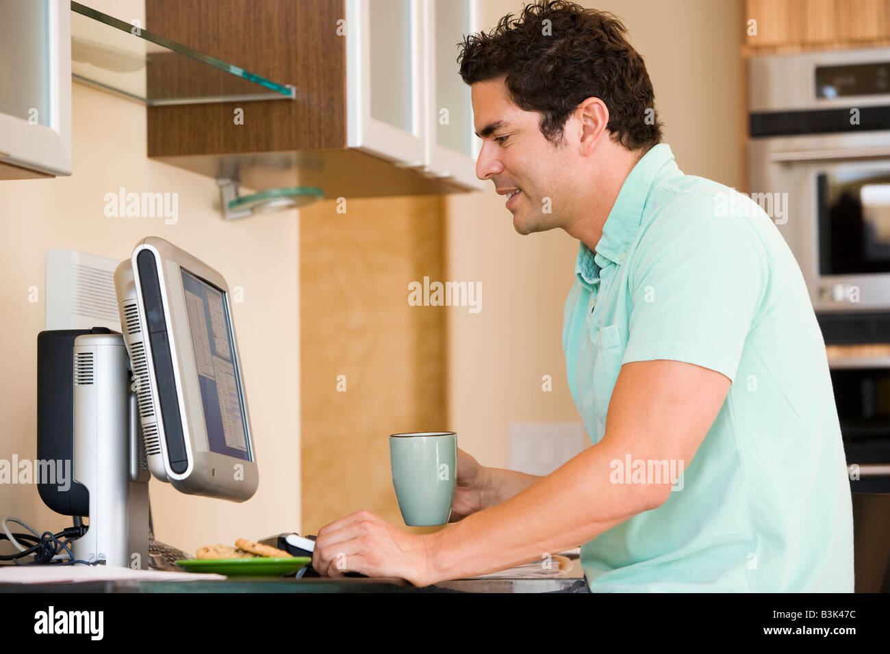 Man in kitchen with coffee using computer and smiling Stock Photo