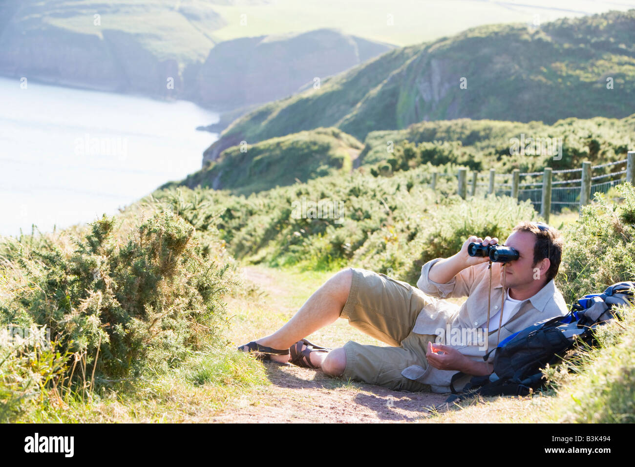 Man relaxing on cliffside path using binoculars Stock Photo