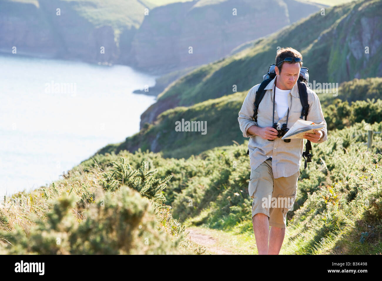 Man walking on cliffside path looking at map Stock Photo