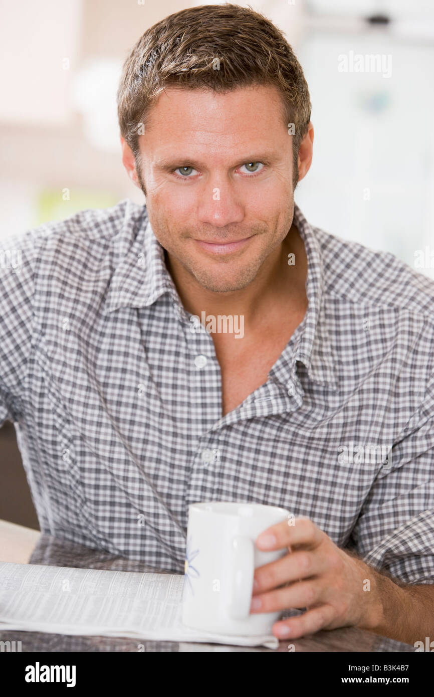 Man in kitchen reading newspaper and smiling Stock Photo