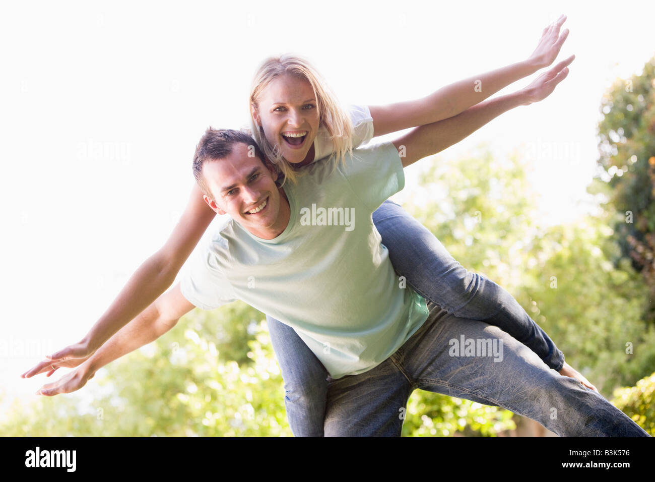Man giving woman piggyback ride outdoors smiling Stock Photo
