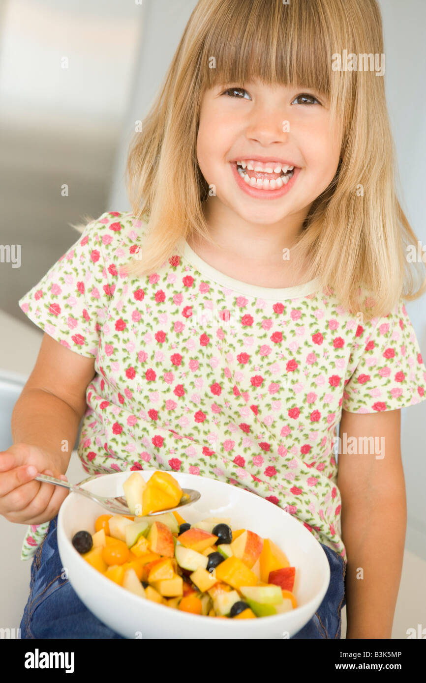 Young girl in kitchen eating bowl of fruit smiling Stock Photo Alamy