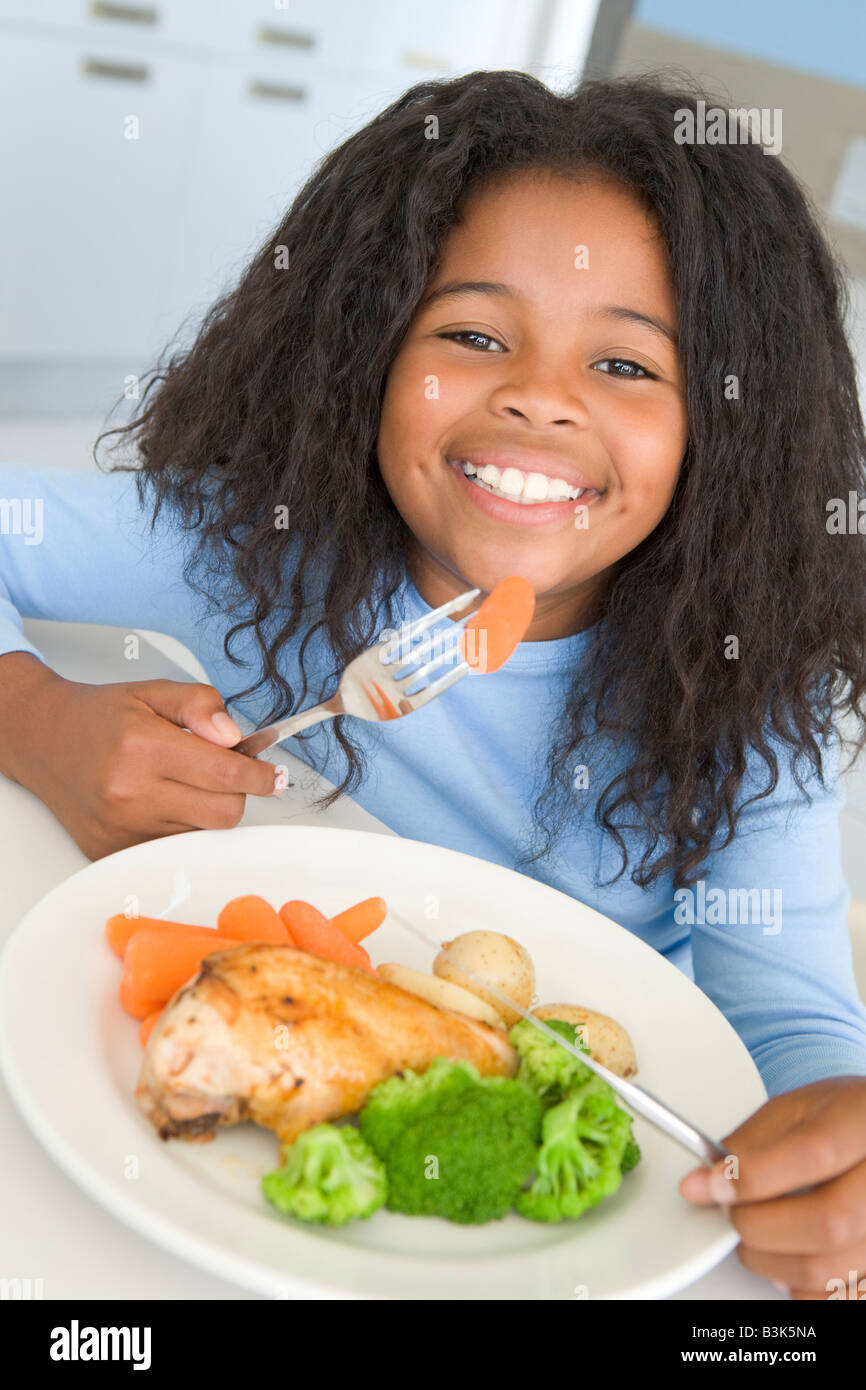 Young girl in kitchen eating chicken and vegetables smiling Stock Photo Alamy