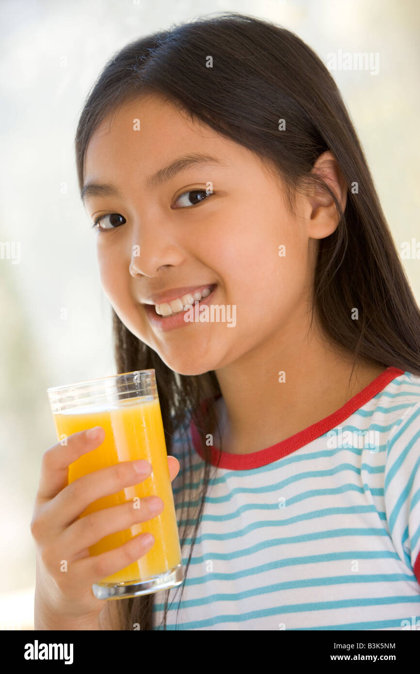 Young girl indoors drinking orange juice smiling Stock Photo - Alamy