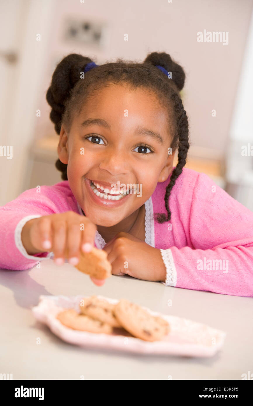Young girl in kitchen eating cookies smiling Stock Photo Alamy