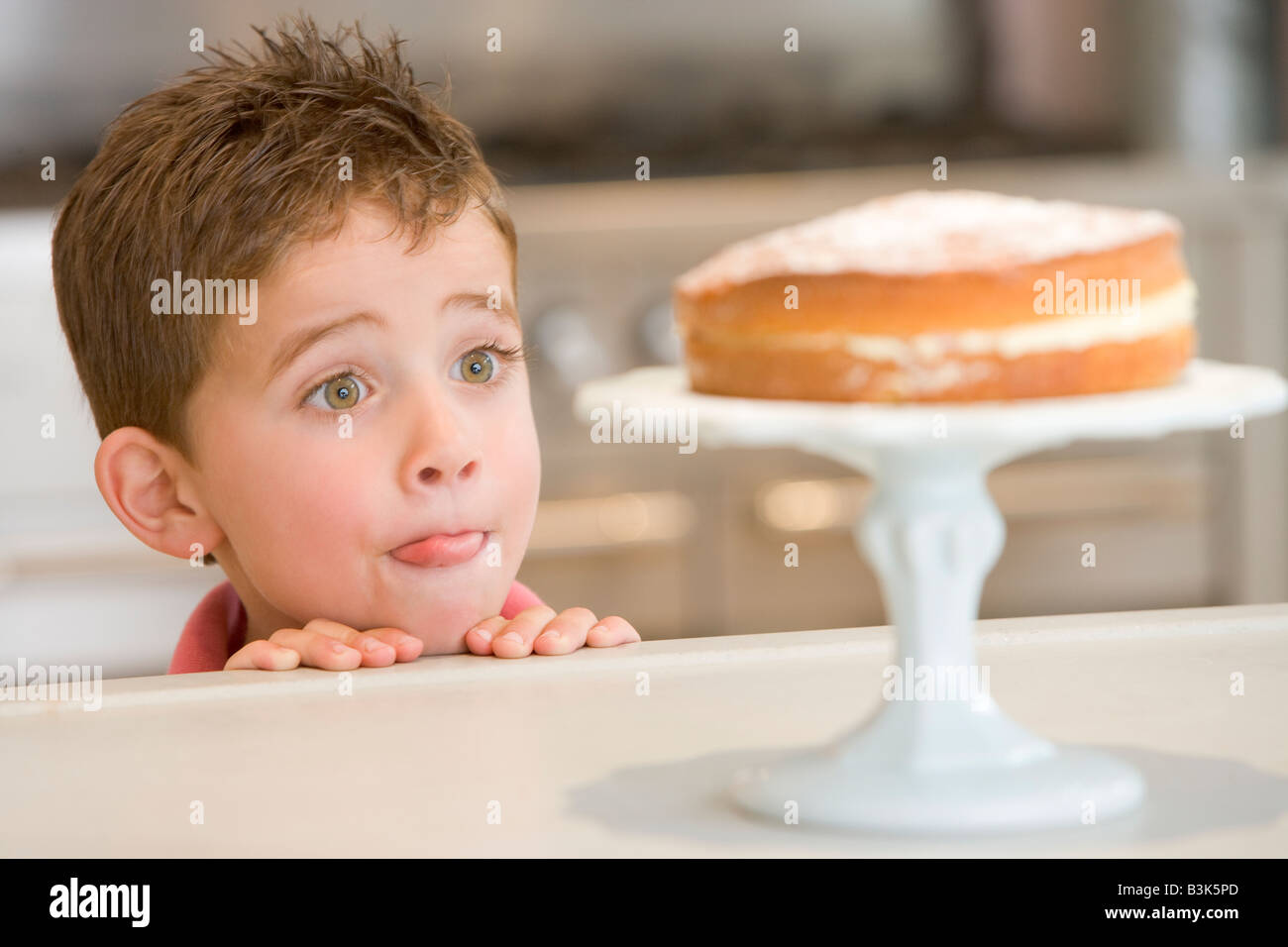 Young boy in kitchen looking at cake on counter Stock Photo