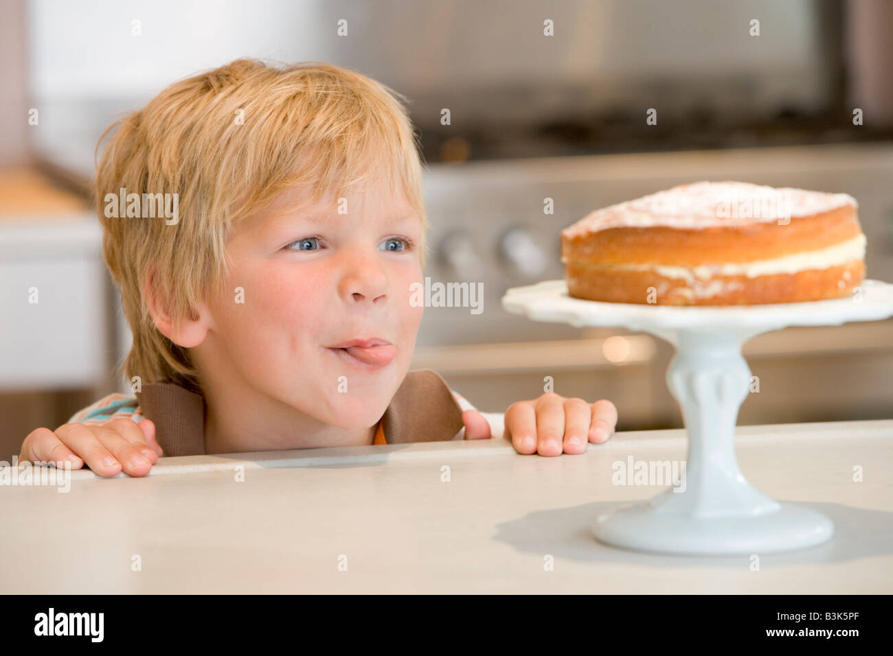 Young boy in kitchen looking at cake on counter Stock Photo
