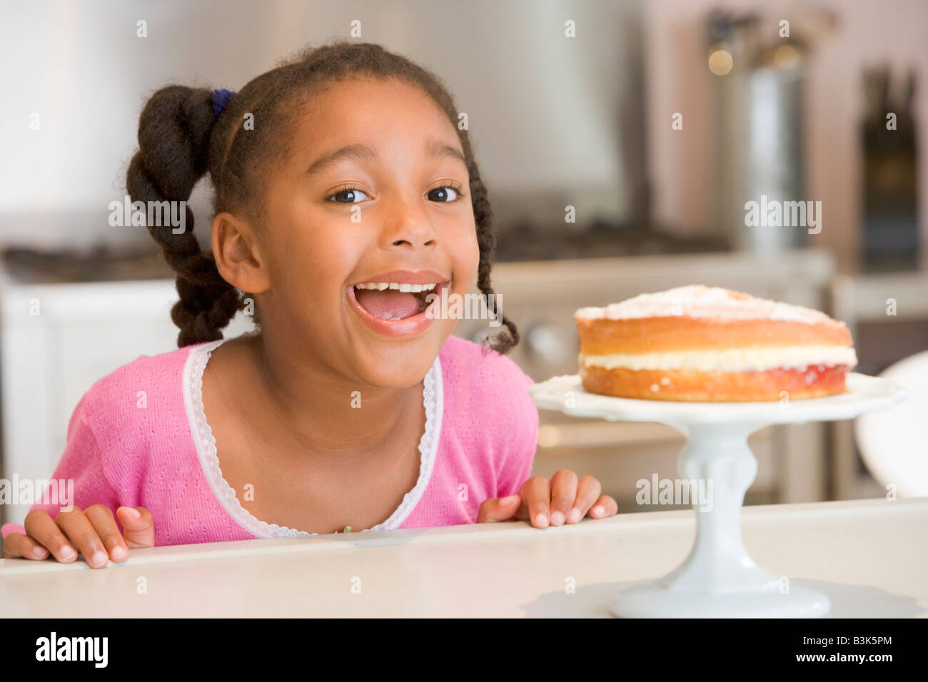 Young girl in kitchen looking at cake on counter smiling Stock Photo