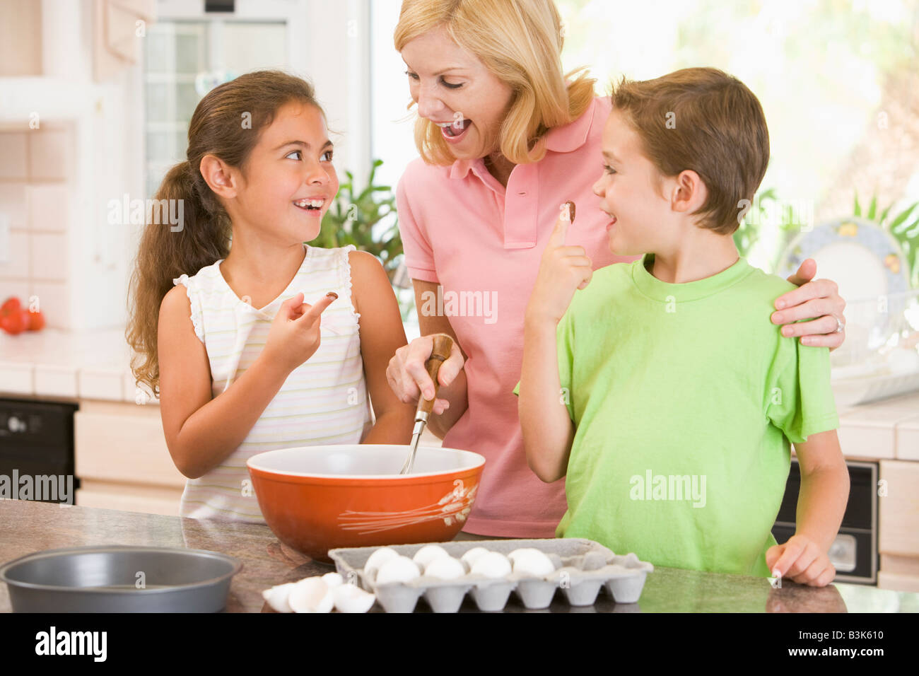 Woman and two children in kitchen baking and smiling Stock Photo