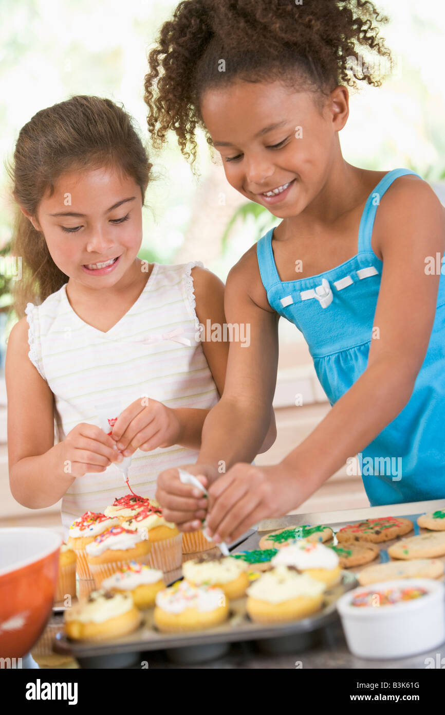 Two children in kitchen decorating cookies smiling Stock Photo