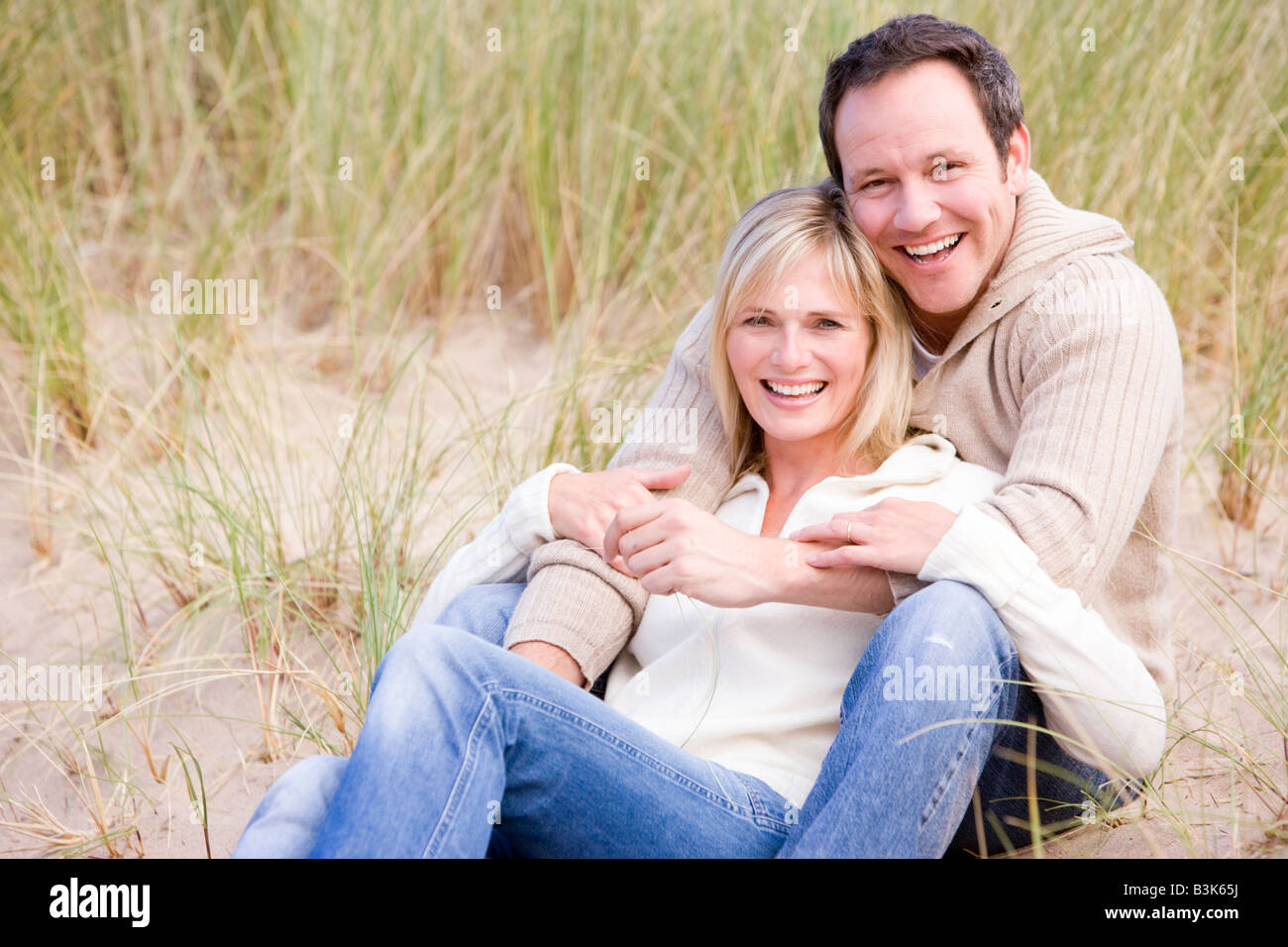 Couple sitting on beach smiling Stock Photo