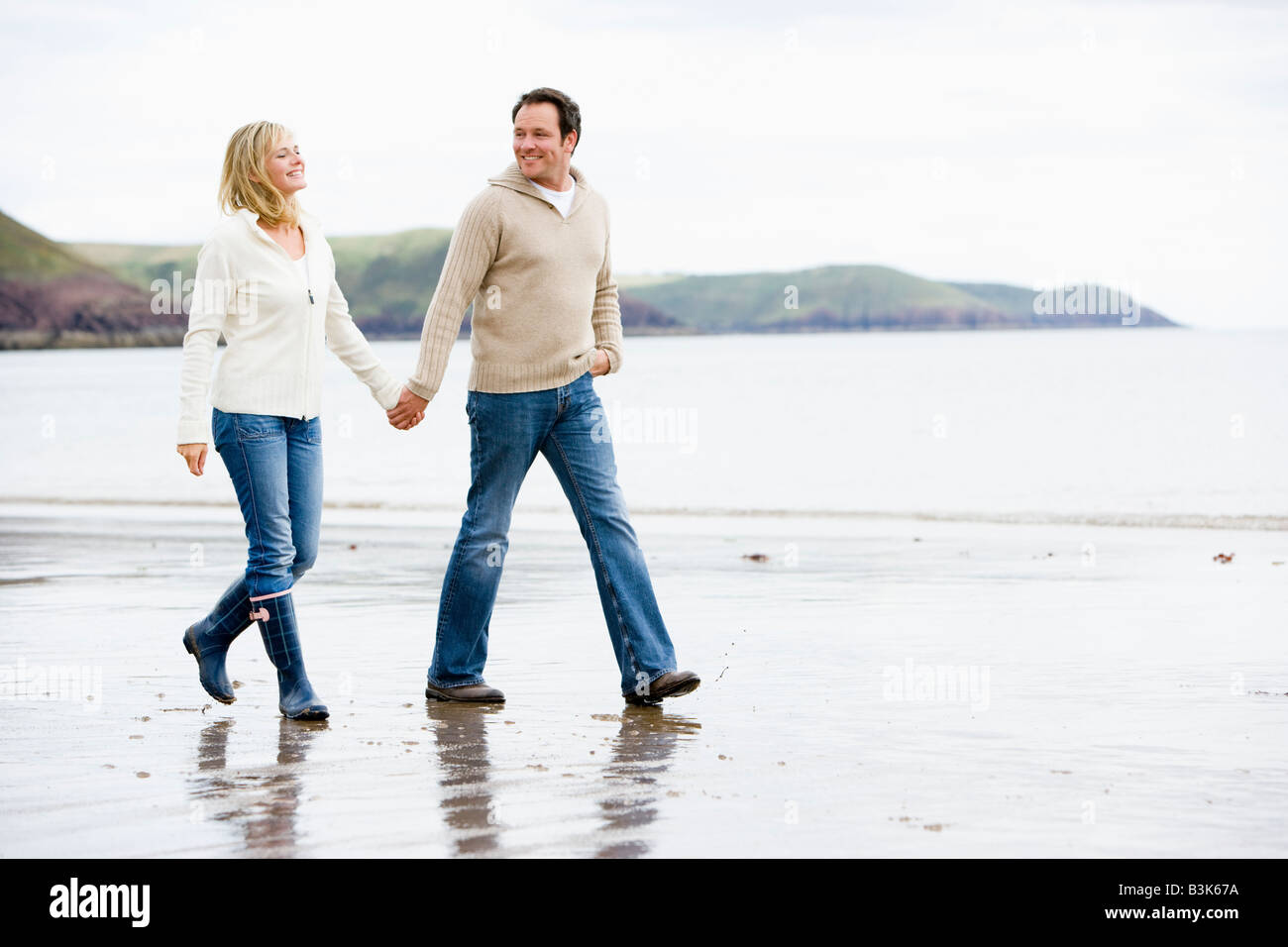 Couple walking on beach holding hands smiling Stock Photo