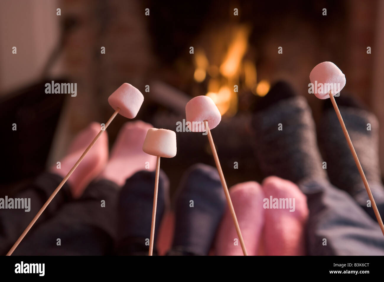 Feet warming at a fireplace with marshmallows on sticks Stock Photo