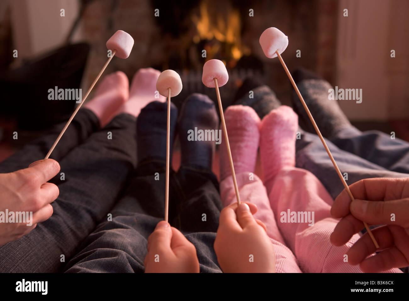 Feet warming at a fireplace with marshmallows on sticks Stock Photo